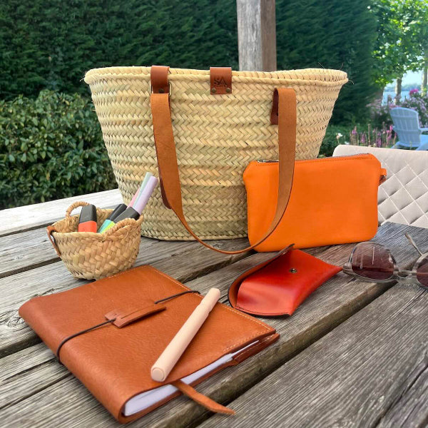 Leren notebook op de tafel met andere leren attributen en een rieten tas