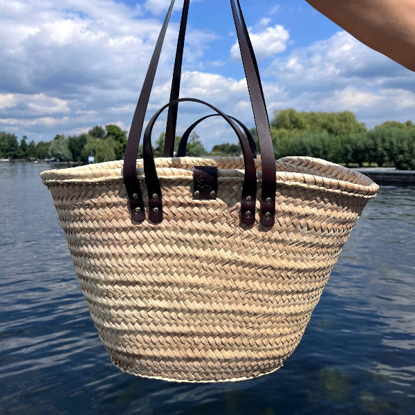 Rieten tas met donkerbruine handvatten en leer en gouden studs boven het water