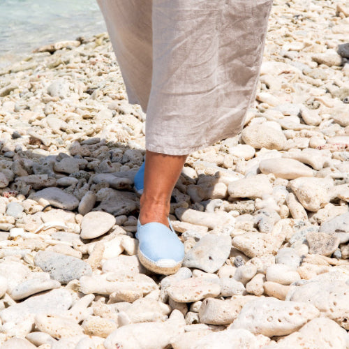 Authentieke Spaanse Espadrilles in lichtblauw aan de voet on beach