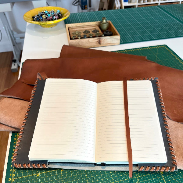 Grijze leren notebook A5 met bruin vlechtwerk en bruin lint als sluiting opengeslagen op werkbank