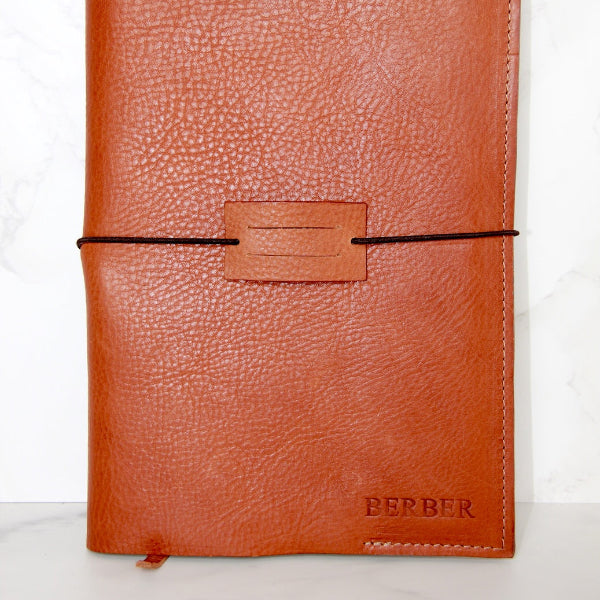 Handgemaakte leren notebook cover in camel met naam tegen de muur