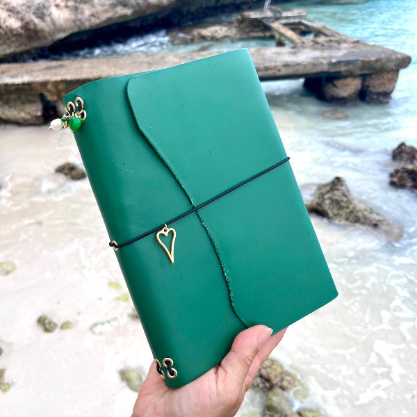 Leren notebook in groen in de hand op het strand