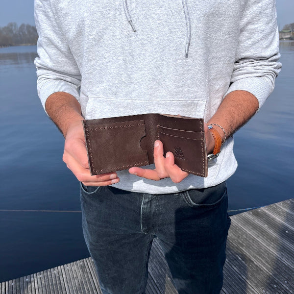 Leren handgemaakte portefeuille in donkerbruin in de hand op de steiger 