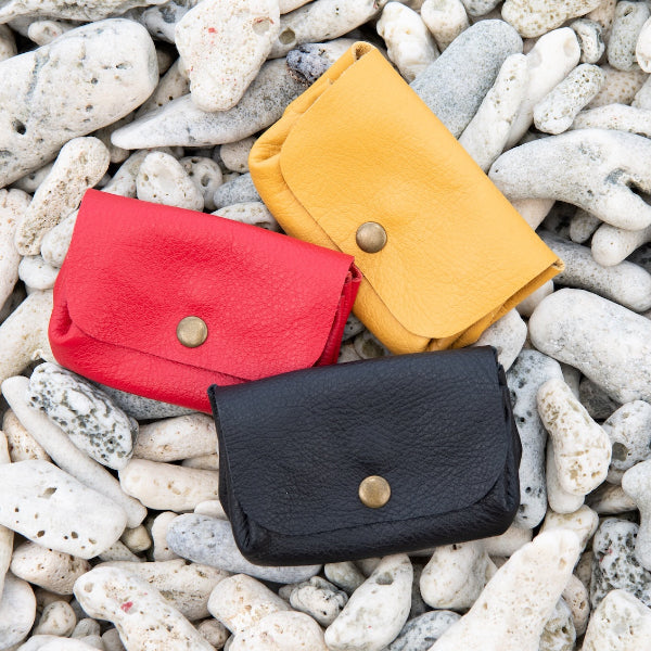 Diverse portemonnees met 3 vakken in zwart, rood en geel op het strand