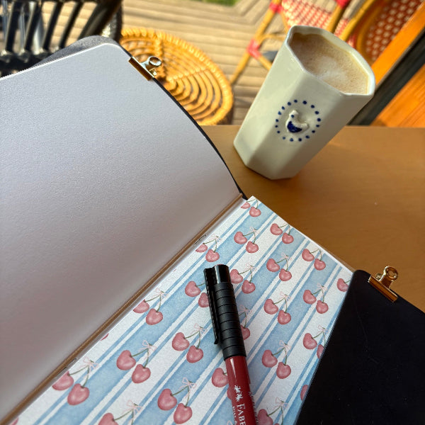 Opengeslagen notebook met bedels in donkerblauw met designpapier en een stift