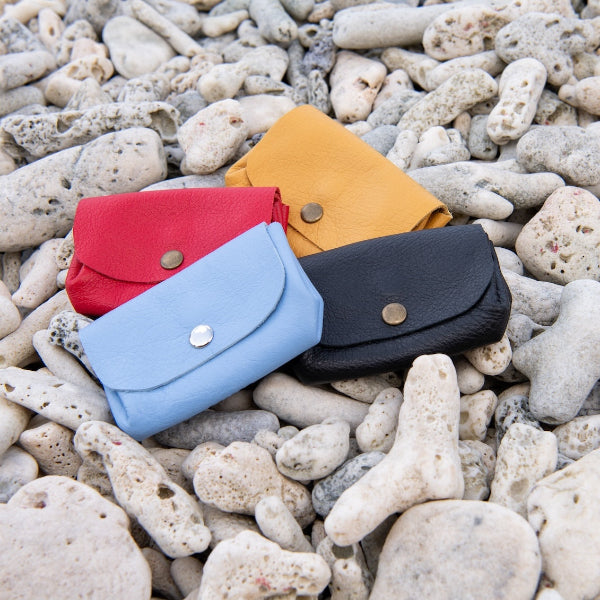 Diverse portemonnees met 3 vakken in lichtblauw, zwart, rood en geel op het strand