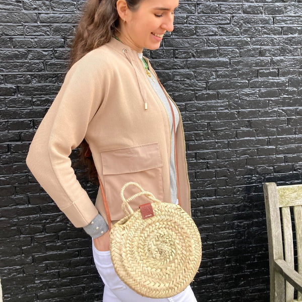 Rieten schoudertas klein gedragen door Sofia in Amsterdam met als achtergrond een zwarte muur