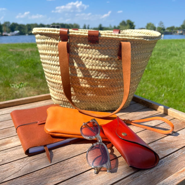 Handgemaakte rieten tas uit de Sevilla collectie met leren accessoires op tafeltje aan het water