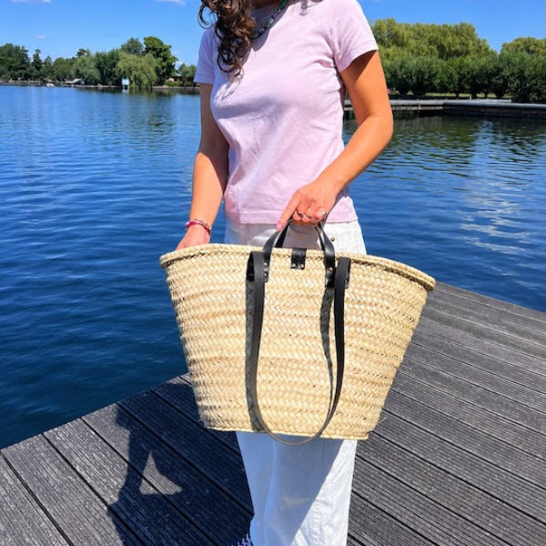 Foto aan de hand van de rieten strandtas medium met zwarte handvatten en hengsels