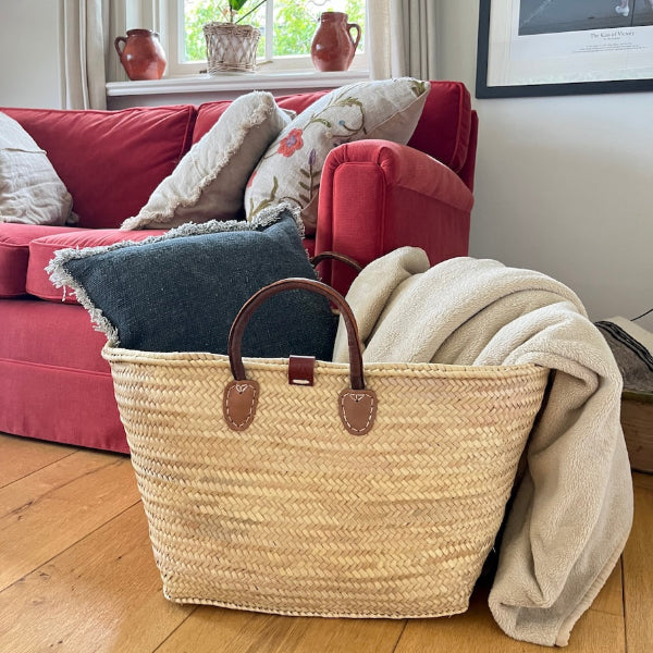 Zeer ruime rieten tas met leren handvatten uit de Valencia collectie met kussens en een plaid in een woonkamer