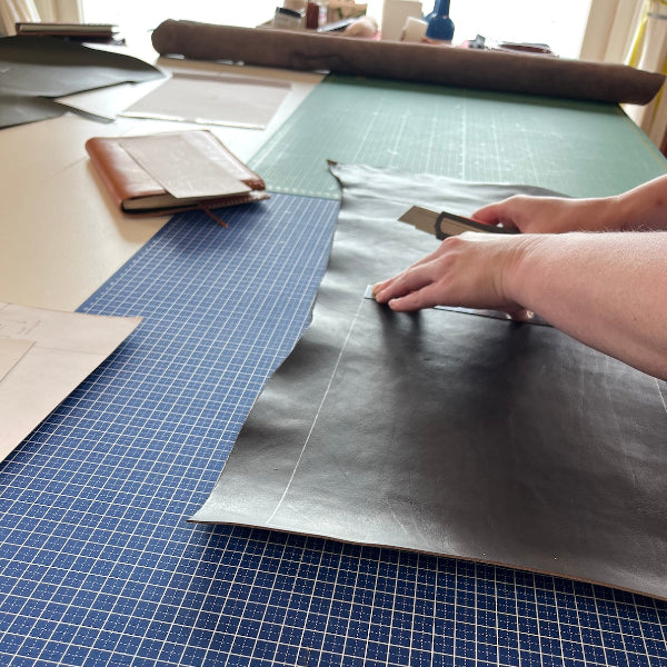 Snijden van onderdelen donkerbruine notebook met roze garen uit workshop van SA Design