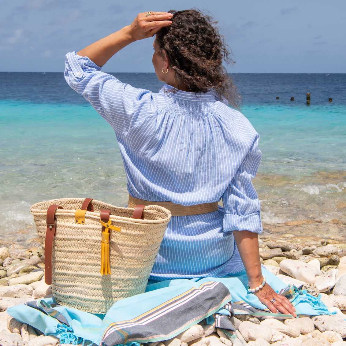 Rieten tas met leren kwast op het strand met een handdoek erin