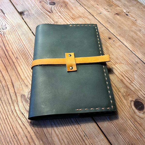 Handgemaakte leren notebook die is gemaakt in een workshop op locatie in groen met gele sluitband