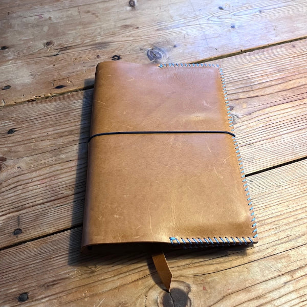 Handgemaakte leren notebook die is gemaakt in een workshop op locatie in zand met blauw garen